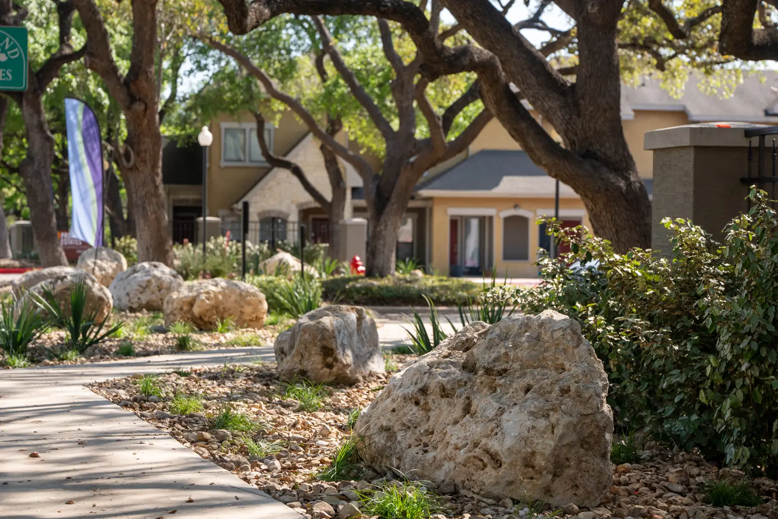 Limestone boulders and planted beds beside a shaded walkway at Providence Estates Townhomes in San Antonio